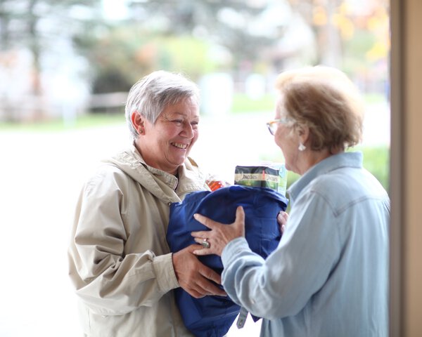 Pflegerin gibt älterer Dame eine volle Einkaufstasche | © Heinz von Haydenaber